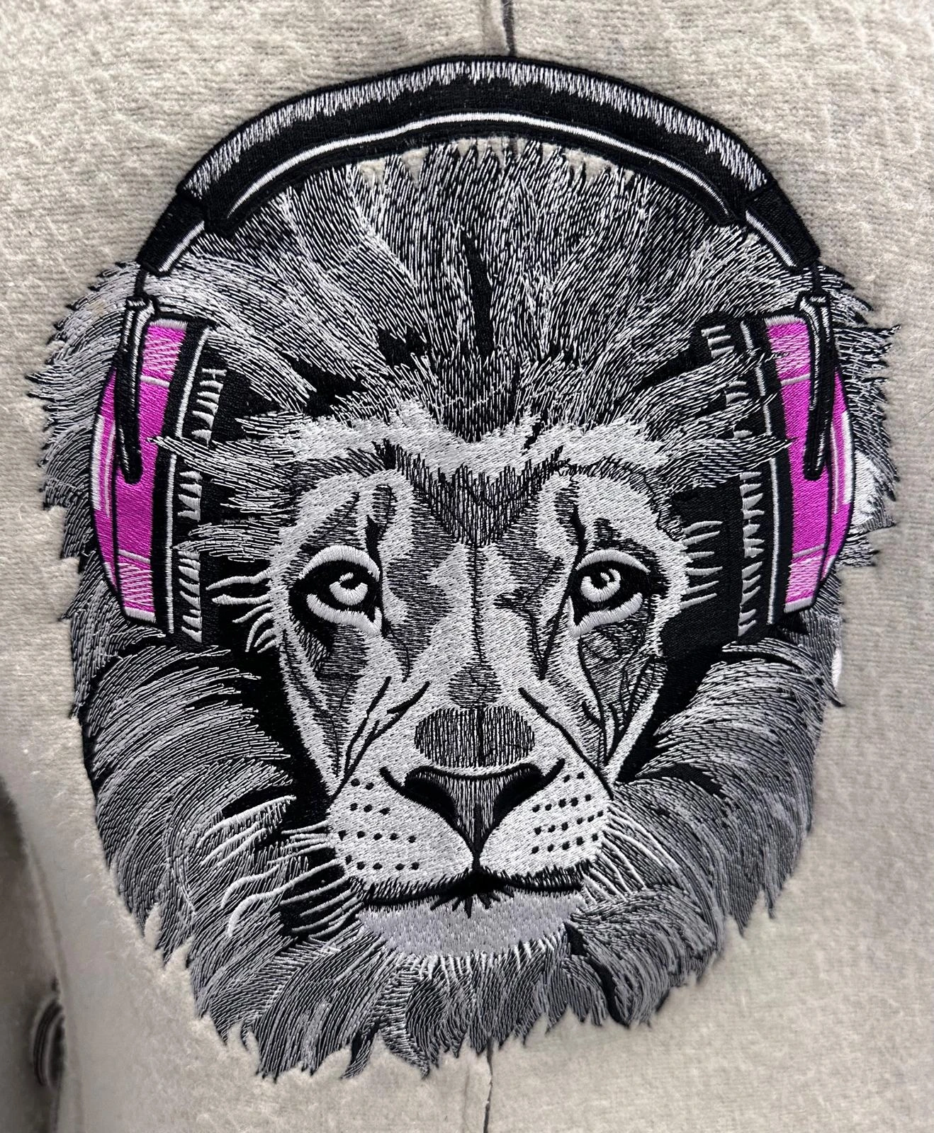 Gros plan d’une tête de tigre brodée en noir et blanc avec un casque rose sur textile gris